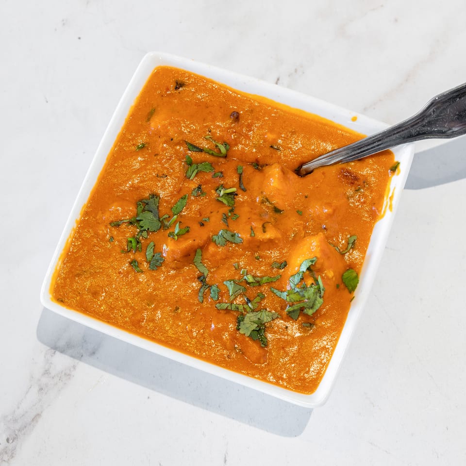 Creamy orange curry garnished with fresh cilantro, served in a white square bowl with a spoon.