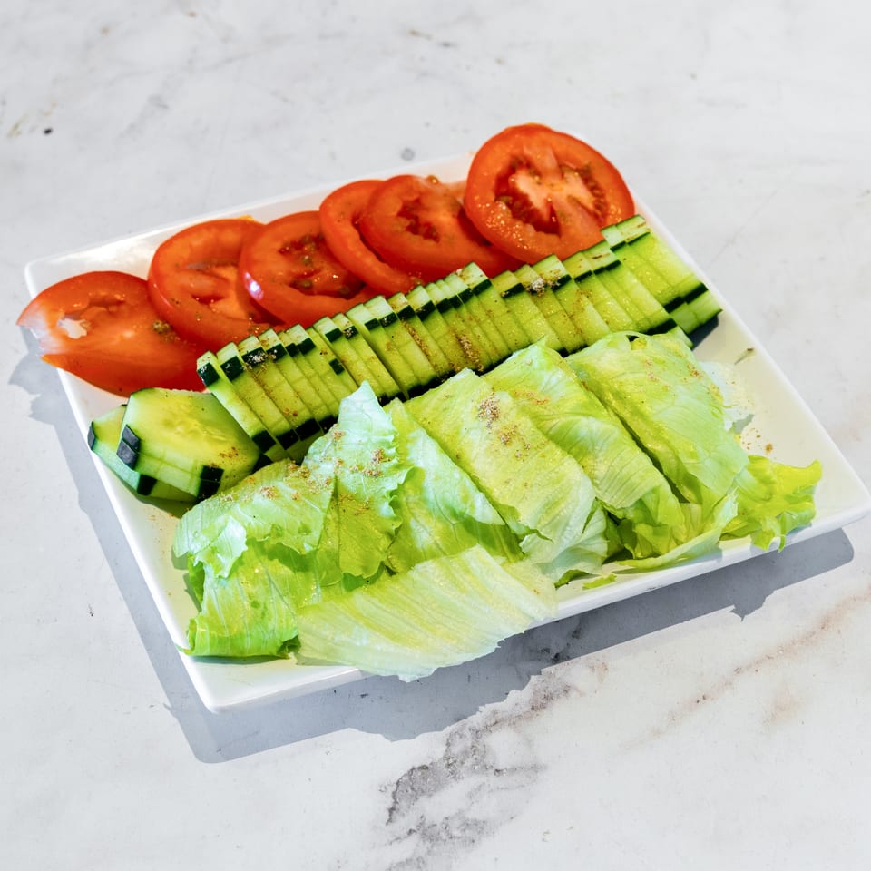 White plate of sliced tomatoes, cucumbers, and lettuce arranged as a fresh seasoned salad.