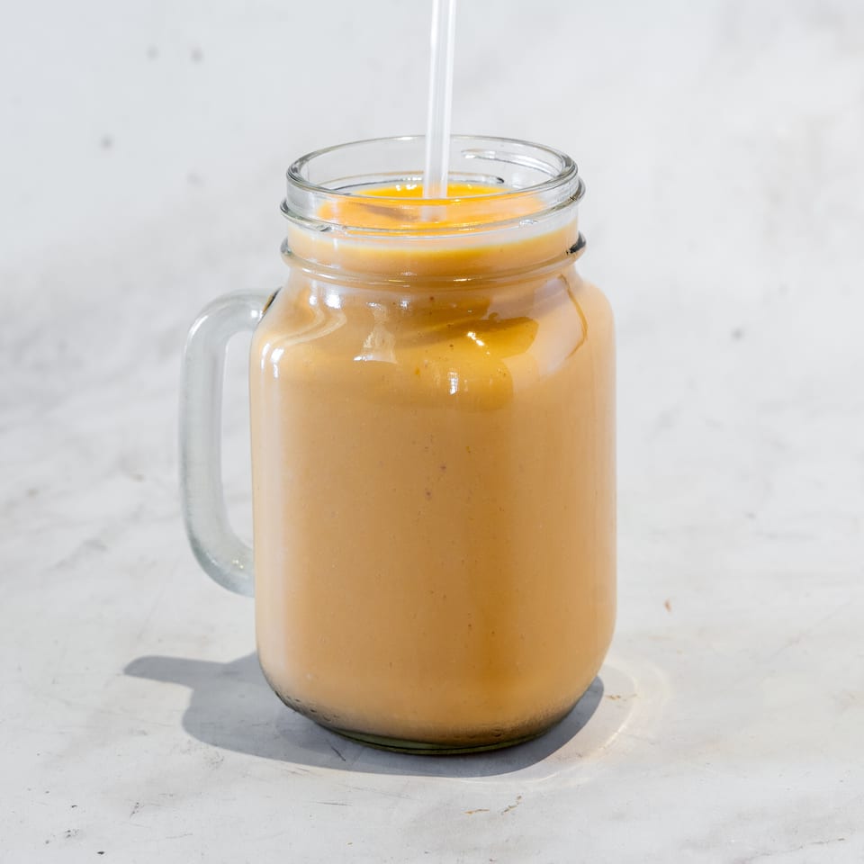 Creamy orange smoothie in a clear glass mason jar with a straw, resting on a sunlit white countertop.