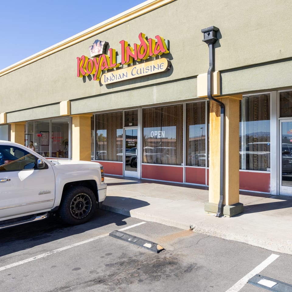 Sunlit storefront of Royal India Indian Cuisine with large signage, glass entrance, parking lot, and a white pickup truck.