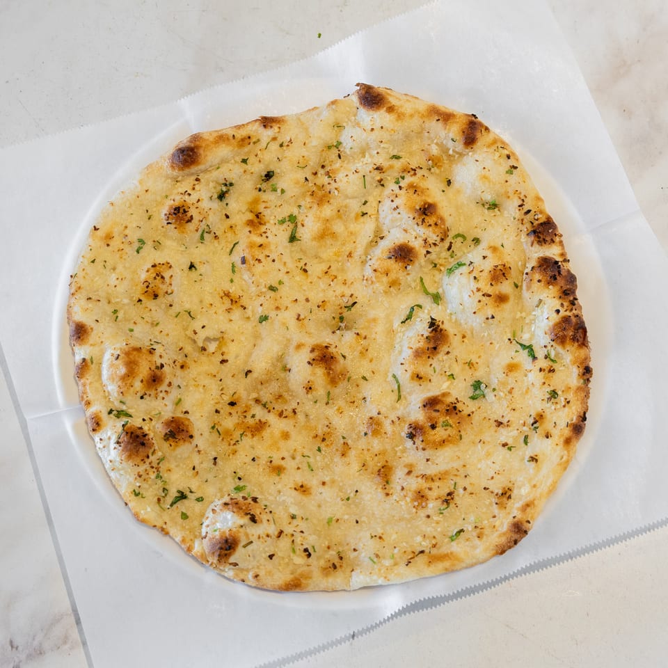 Golden garlic flatbread sprinkled with herbs, served on parchment paper.