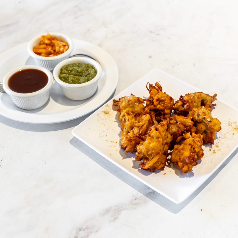 Golden vegetable fritters served on a white platter with three dipping sauces in ramekins.