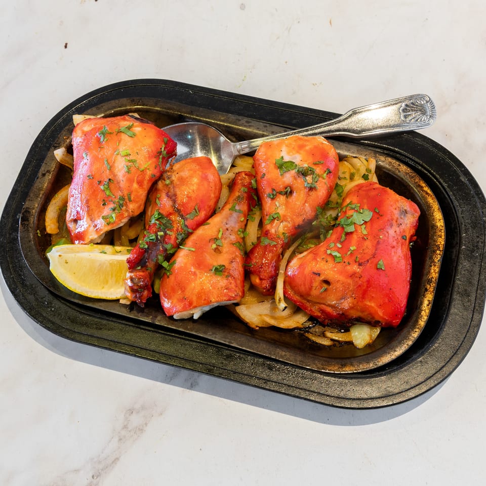Tandoori chicken pieces garnished with cilantro, served with sautéed onions and lemon on a sizzling platter.