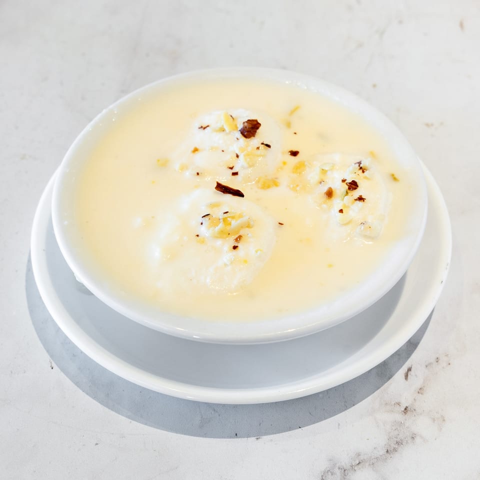 White bowl of creamy soup topped with dollops of cream, crumbled cheese, and red pepper flakes on a saucer.