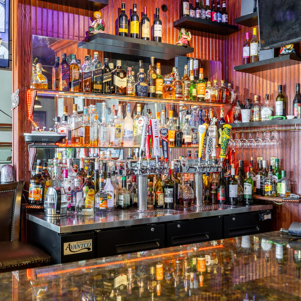 Fully stocked restaurant bar with liquor bottles, beer taps, hanging glasses, wood paneling, and televisions.