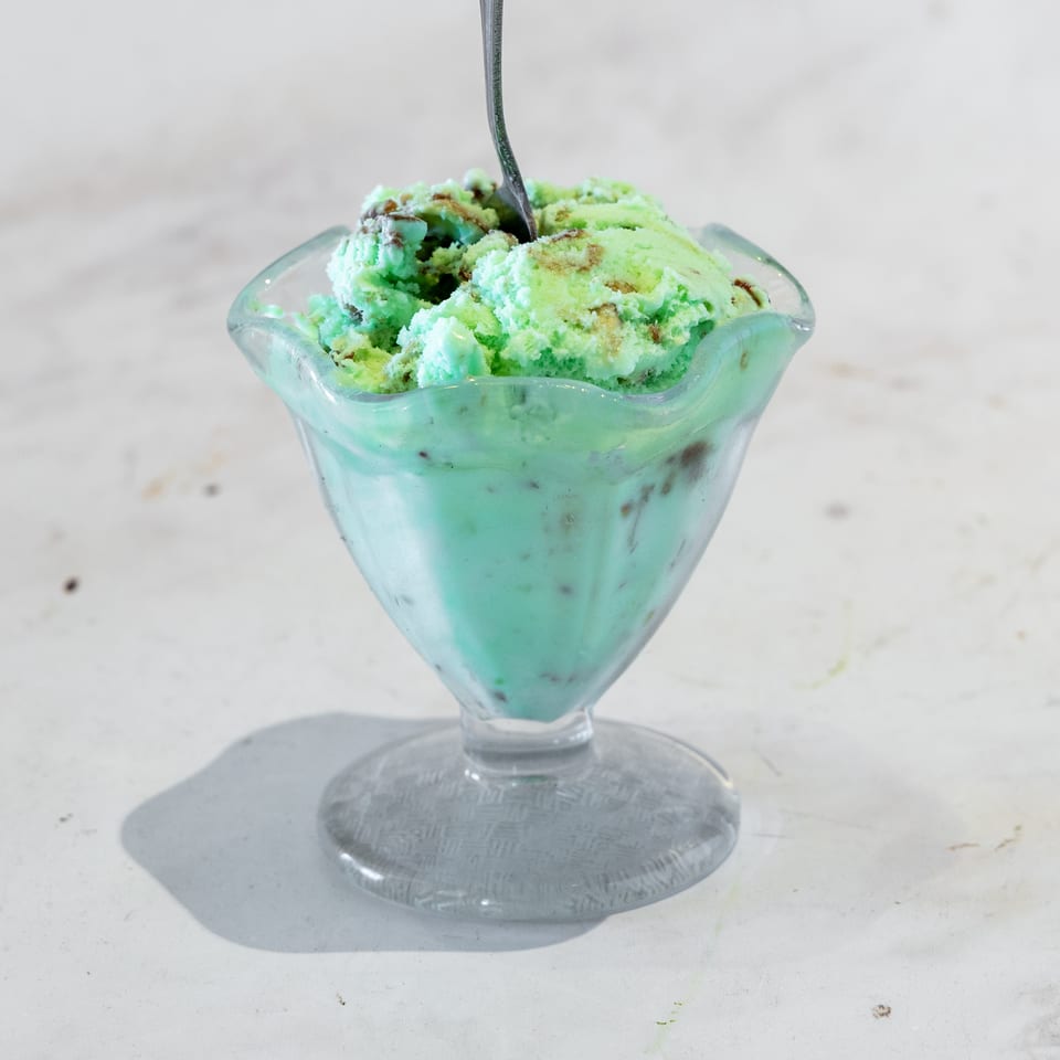 Mint-green ice cream with chocolate swirls in a scalloped glass dessert cup and spoon.