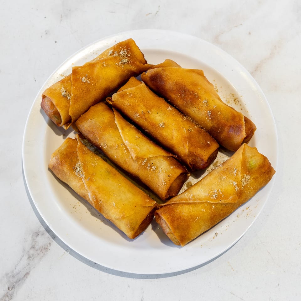Plate of golden-brown fried spring rolls dusted with seasoning on a white tabletop.