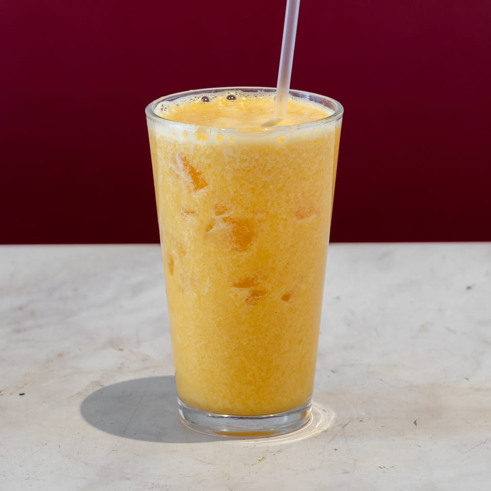 Frosty orange beverage in a clear glass with a straw, displayed on a marble counter against a burgundy background.