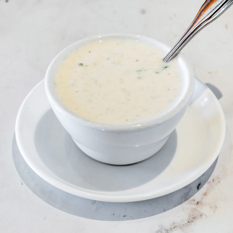 Creamy herb-speckled soup in a white bowl with a spoon, resting on a matching saucer.