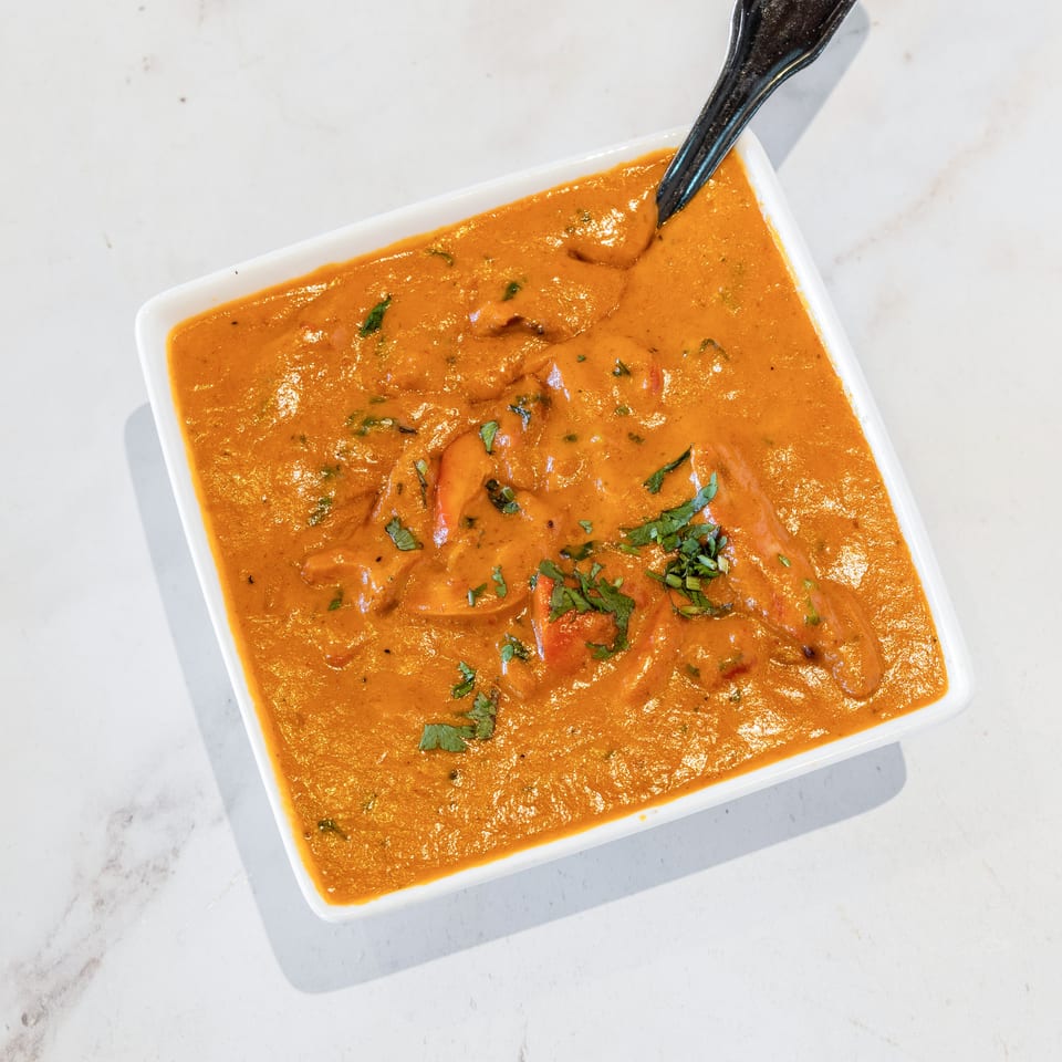 Creamy orange curry with chunks of vegetables and fresh cilantro, served in a white square bowl with a spoon.